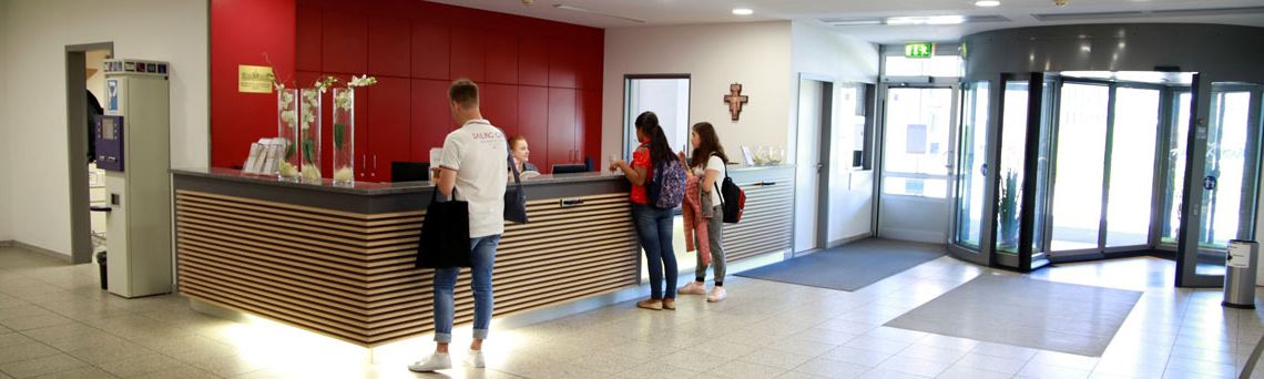 Patienten und Besucher stehen am Informationsdesk im Haupteingang und sprechen mit dem Servicepersonal. 