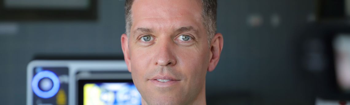 Dr. Armin Secker im grünen OP Kasack vor einem Laser im Operationsraum. 