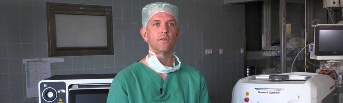 Dr. Armin Secker im grünen OP Kasack vor einem Laser im Operationsraum. 