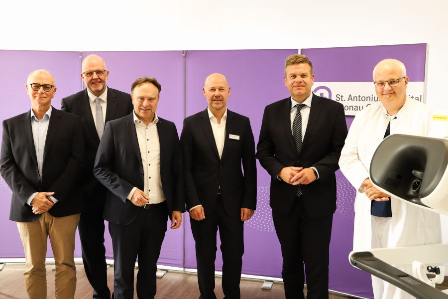 Von links: Patient Bernd Loeffler, Senior Vice President Dirk Barten (Intuitive), Landrat Dr. Kai Zwicker, Geschäftsführer Christoph Bröcker (St. Antonius-Hospital), Staatssekretär Matthias Heidmeier (Ministerium für Gesundheit, Arbeit, Soziales NRW) und Chefarzt Dr. med. Christian Wagner (St. Antonius-Hospital) neben der Konsole des neuen da Vinci 5 Operationssystems.